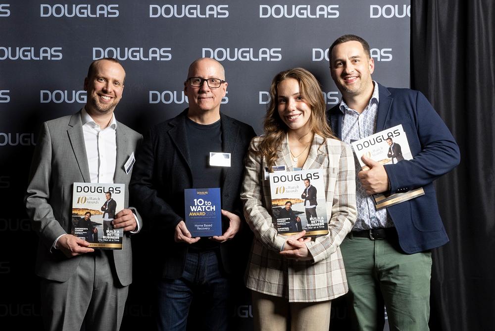 Michael Walsh, wearing glasses, holds an award with three collegues, posing for a photo for Douglas Magazine.