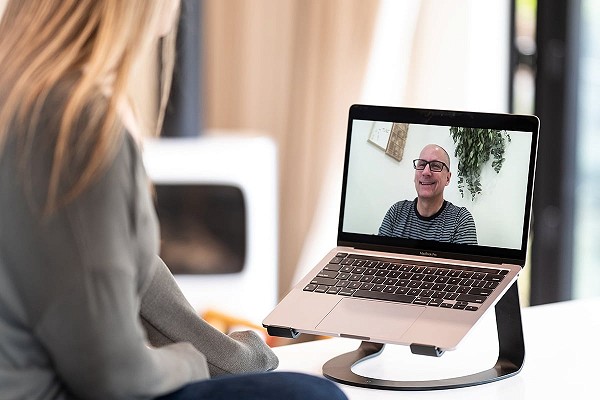 A middle-age woman is talking to an online recovery coach via a laptop video chat; the coach is wearing glasses and looks friendly