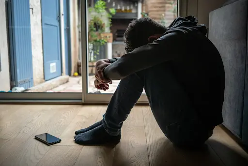 Man sitting on the floor, showing distress.