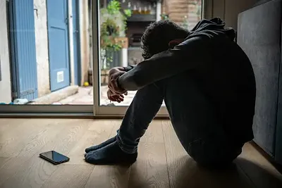 Man sitting on the floor, showing distress.